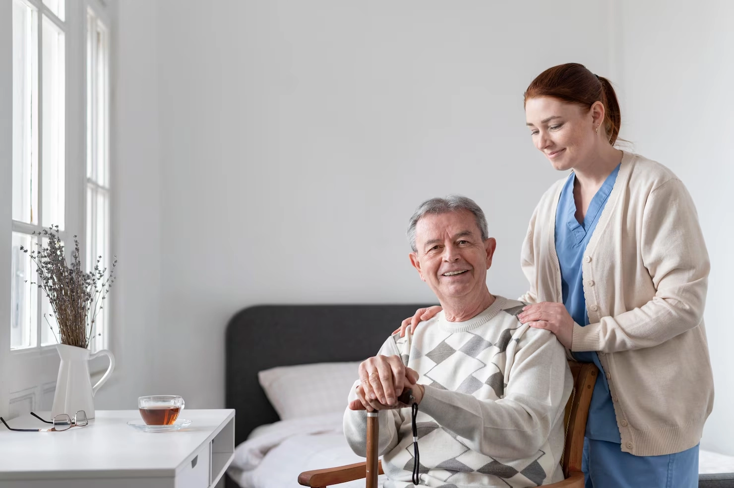 elderly man sitting with a cane and a healthcare worker standing beside him
